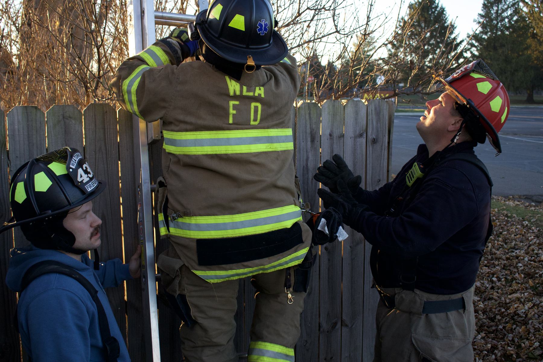 Three firefighters steadying a ladder against a fence