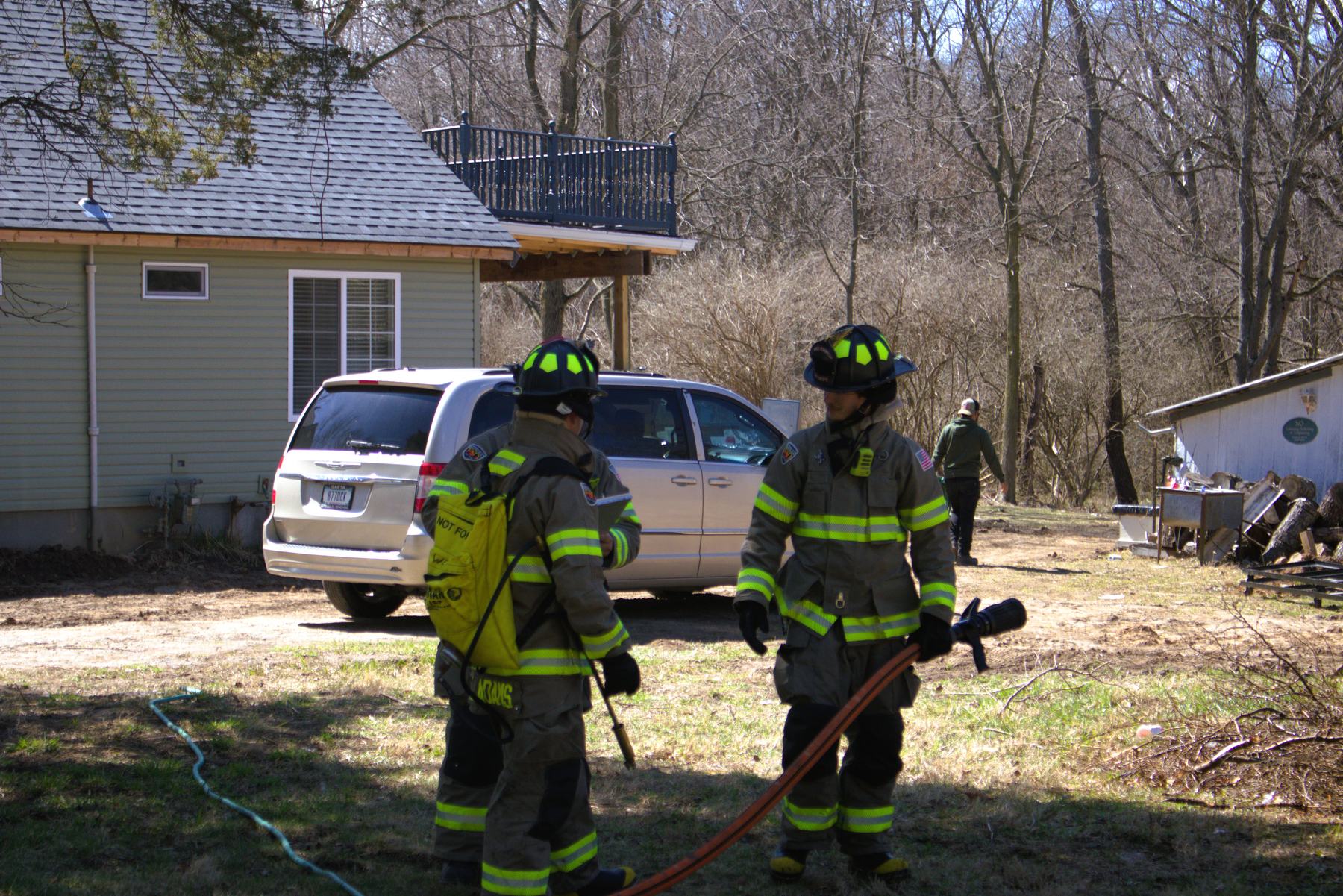 Three firefighters with a hose line beside a house