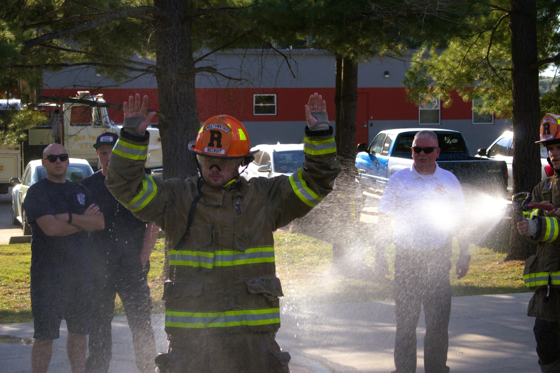 Firefighter with arms raised being rinsed with water