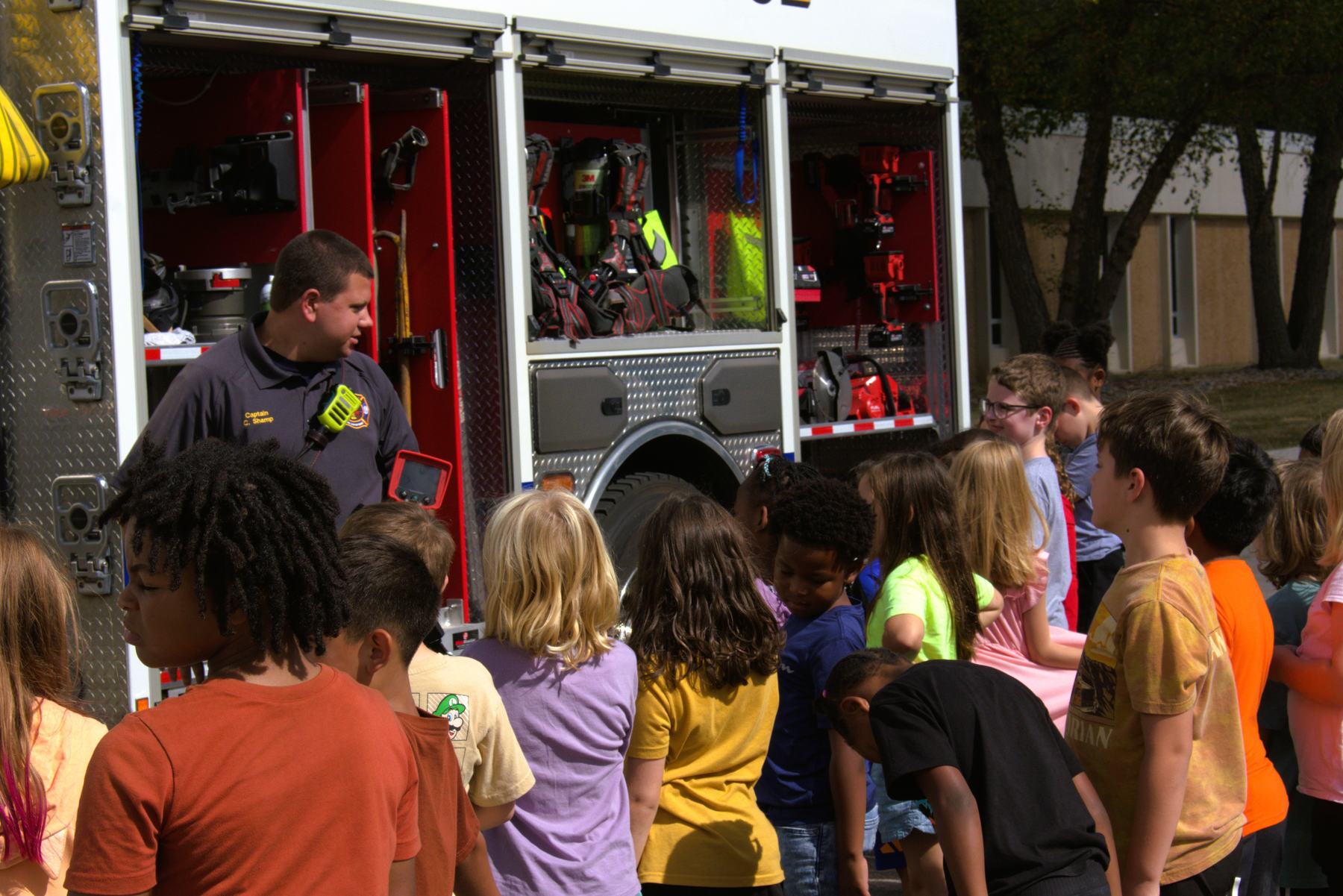 Firefighter showing students the equipment compartments on the engine